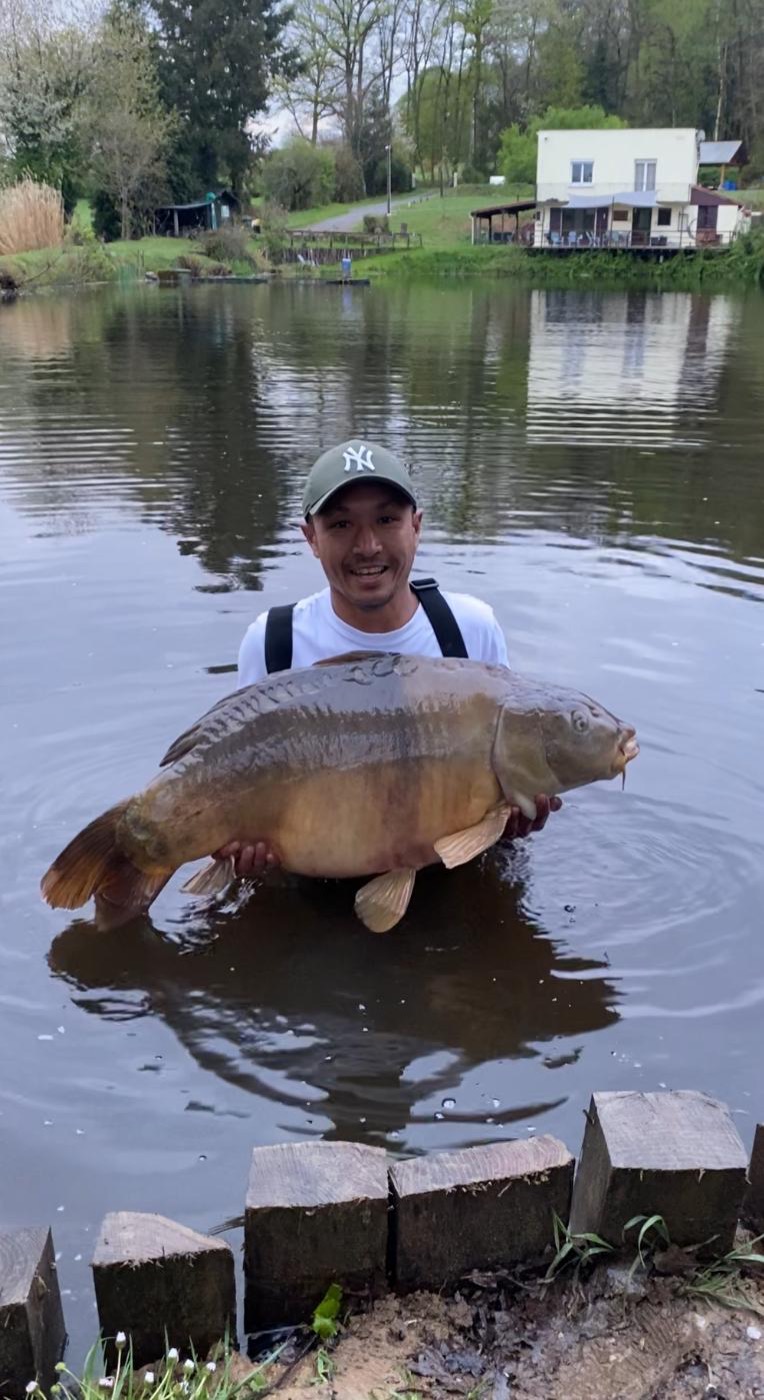 48lb mirror carp held in the lake with the lodge behind, Lodge Lakes
